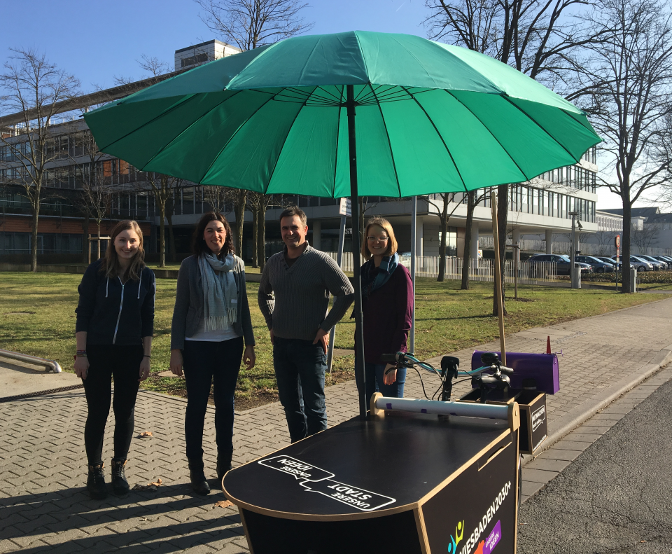 Das Dialog-Mobil zu Wiesbaden 2030+; Foto: Stadtplanungsamt Vier Personen stehend hinter Dialog-Mobil